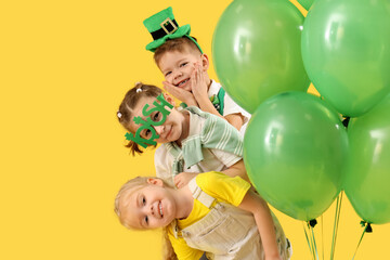 Cute kids with festive green outfits and balloons on yellow background. St. Patrick's Day...