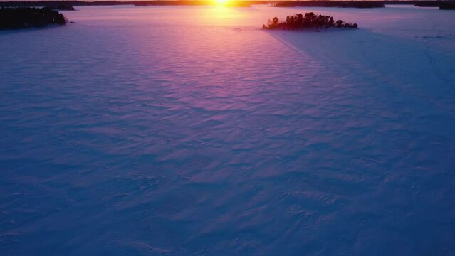 Drone tilting over frozen sea, toward islands and the sunset, winter in Finland