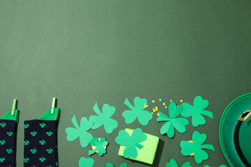 Paper clover leaves on golden coins, gift box, hat and socks on green background, space for text
