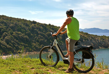 A middle-aged man in denim shorts and a green tank top on an electric bicycle stops and admires the...