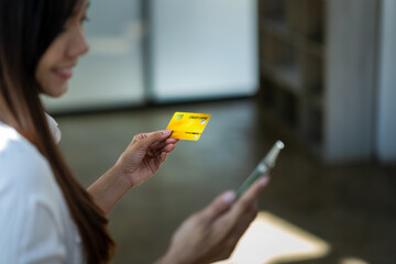 Smiling young woman using smartphone and holding credit card, potentially making an online purchase..