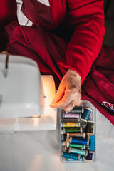 detail vertical of hand of artisan seamstress next to spools of colored threads on sewing machine