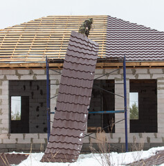 Workers install tiles on the roof of a house in winter