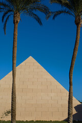 Building is an imitation of an Egyptian pyramid next to palm trees. Construction in the style of an ancient wonder of the world in Africa