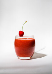 Glass with strawberry, red smoothie and on a white background. There's a cherry on the glass. Summer drink. Vitamins, diet, proper nutrition, vegan