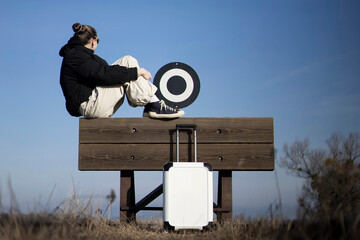 woman or girl with suitcase waiting and sitting on a buffer stop outdoors in nature