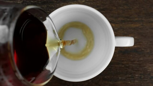Pouring black tea in white cup, top view