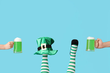 Female legs in green stockings with leprechaun's hat and glasses of beer on blue background. St....
