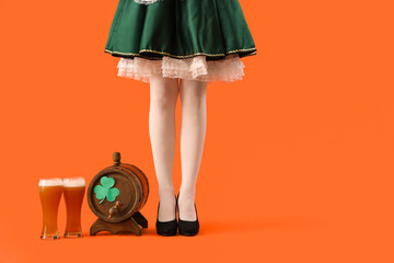 Woman in waitress costume with barrel and glasses of beer on orange background. St. Patrick's Day...