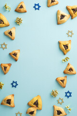 Festive Purim spread. Vertical top view featuring triangular cookies, Star of David motifs, and gold ribbon stars on a soft blue surface, with space for wording