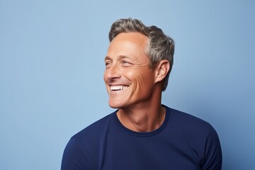 Portrait of a handsome middle-aged man smiling against blue background - obrazy, fototapety, plakaty