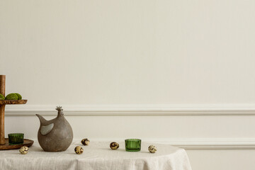 Minimal spring composition of easter living room interior with copy space, beige wall with stucco hen sculpture, green glass, quail eggs and personal accessories. Home decor. Template.