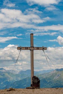 Wooden cross marking the Blaser peak 2241 m in the Stubai Alps above the village of Trins, Tyrol, Austria, alpine landscape and blue sky with white clouds in the background.