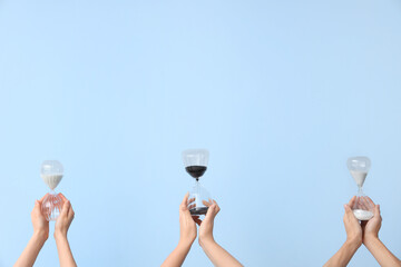 Female hands holding hourglasses on blue background