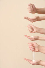 Many hands with pouring sand on beige background. Time concept