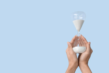 Female hands holding hourglass on blue background