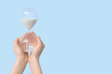 Female hands holding hourglass on blue background