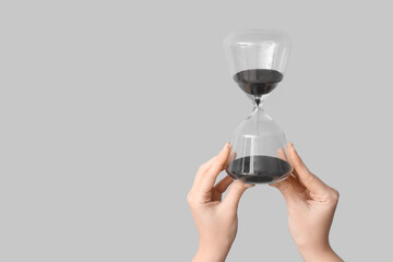 Female hands holding hourglass on grey background