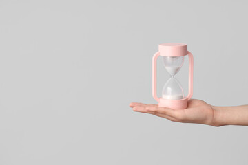 Female hand holding hourglass on grey background