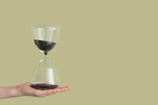 Female hand holding hourglass on green background
