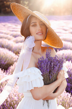 A young girl,beautiful woman portrait in lavender field in white dress and straw hat holding a bouquet of lavender flowers.Front view of beautiful girl in a white dress and hat in a lavender field