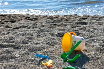 Children's toys on the seashore, a bucket, a scoop, a rake lie on a rocky beach. Child safety concept.