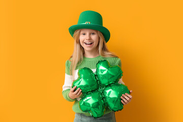 Cute little girl in leprechaun hat with air balloon in shape of clover on yellow background. St....