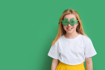 Cute little girl in decorative glasses in shape of clover on green background. St. Patrick's Day...