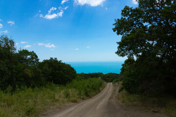 Fototapeta premium Mountain country road leading to the sea from a milestone to the bottom against the sky.