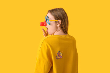 Beautiful young shocked woman with paper fish attached to her back on yellow background. April...