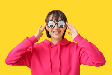 Beautiful young woman in funny disguise on yellow background. April Fools Day celebration