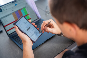 Close up view of man hand holding smart phone and stylus pen at his creative workspace. 