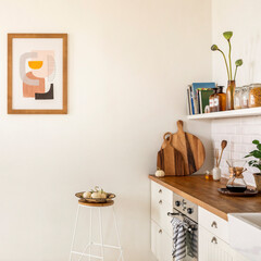 Minimalist composition of kitchen interior with mock up poster frame, white kitchen furniture, wooden kitchen island, induction hob, stool with bowl, pear and personal accessories. Home decor Template