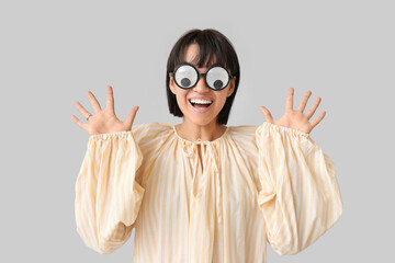 Beautiful young happy woman in funny disguise on grey background. April Fools Day celebration
