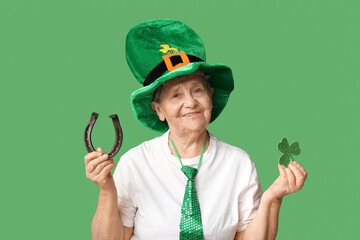 Senior woman in leprechaun hat with horseshoe and clover on green background. St. Patrick's Day...