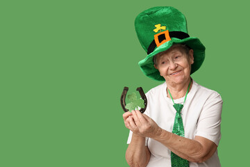 Senior woman in leprechaun hat with horseshoe and clover on green background. St. Patrick's Day...