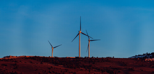 : A striking vista of modern wind turbines, stationed amidst the mountainous terrain, exemplifying...