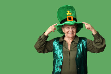 Senior woman pointing at leprechaun hat on green background. St. Patrick's Day celebration