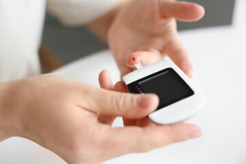 Diabetic woman with glucometer measuring blood sugar level in kitchen, closeup