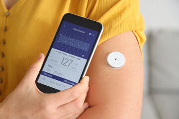 Diabetic woman with glucose sensor using mobile phone for measuring blood sugar level at home, closeup