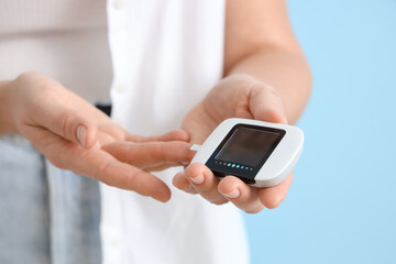 Diabetic woman using glucometer on blue background, closeup