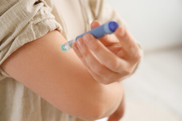Diabetic woman using lancet pen in bedroom, closeup