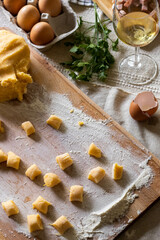 Ingredients like eggs, flour, pancetta and wine on a wooden surface for recipe preparation of gnocchi pasta
