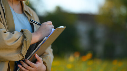 Cropped shot of female farmer writing notes in notepad and examining progress of plants in the field