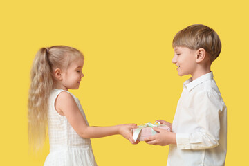 Cute little children with gift box on yellow background. International Women's Day