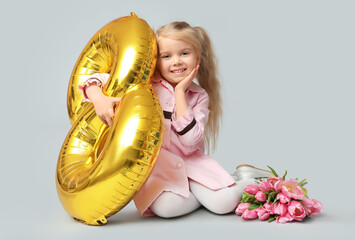 Cute little girl with golden air balloon in shape of figure 8 and bouquet of beautiful tulips on grey background. International Women's Day