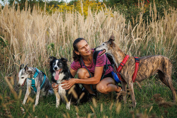 Woman with her dogs resting during dog walking outdoors. Female pet owner or animal trainer doing...