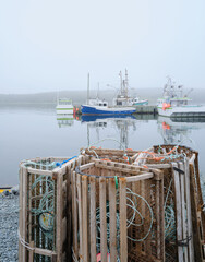 Calm waters of the Hawbolt Cove and several docked lobster boats with wooden lobster pots or traps in thick fog - 729925373
