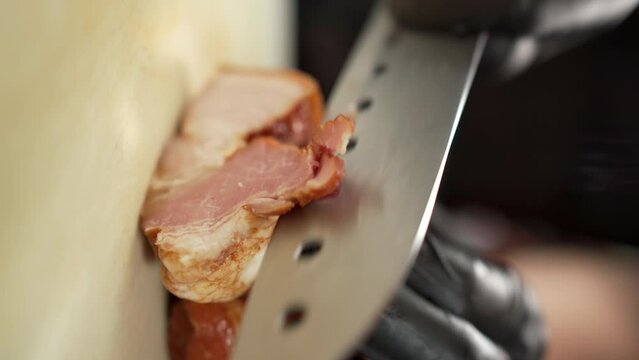 Close-up of a chef cut smoked bacon into thin slices on cutting board with a sharp Chinese knife. Bacon is one of the favorite additions to eggs and hamburger
