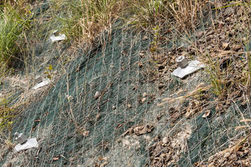 Erosion protection mesh stabilizing a sloped ground surface to prevent potential landslides along...